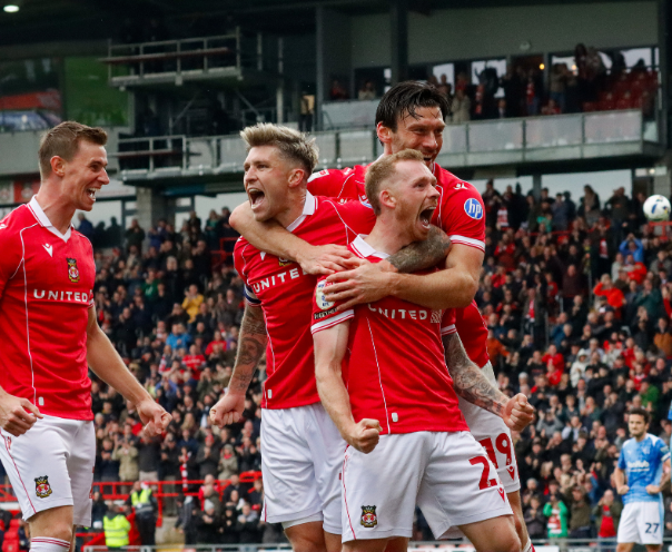 Group of soccer players in red jerseys celebrating on the field with a crowd in the background