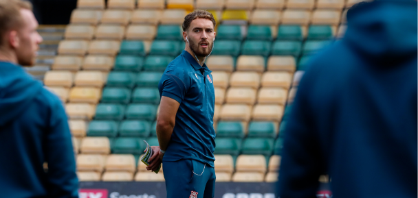 Man in sports uniform standing on a field with stadium seats in the background